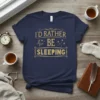 I'd Rather Be Sleeping quote in gold distressed font on a navy blue t-shirt, with moon and stars graphic