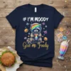 If I'm Moody Give Me Foody t-shirt with a raccoon astronaut drinking a milkshake, surrounded by butterflies and burgers