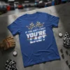 Blue t-shirt with "IF YOU AIN'T FIRST YOU'RE LAST" text and checkered flags graphic, suitable for racing fans