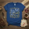 White and gold script typography design on a navy blue t-shirt that reads "if you think MY HANDS are full