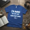 Blue t-shirt with white and blue text that reads "I'M AWAKE BUT NOT LIKE DOING STUFF AWAKE" and a sleepy