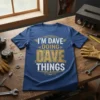 Blue t-shirt with "I'M DAVE DOING DAVE THINGS" text in white and gold distressed font, featuring vintage wings and decorative