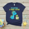Navy blue t-shirt with "I'm Getting A Baby Sister" text and cute blue and green dinosaurs, one hatching from an