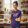 T-shirt with white text "I'm Just Here For The Biscuits" on a purple shirt, worn by a woman holding biscuits