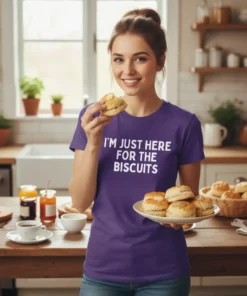 T-shirt with white text "I'm Just Here For The Biscuits" on a purple shirt, worn by a woman holding biscuits