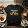 Black t-shirt with white and yellow text that reads "I'm Just Here For The Food" - a funny foodie slogan