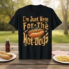 Black t-shirt with bold yellow text "I'm Just Here For The Hot Dogs" and a graphic of a hot dog