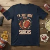 Navy t-shirt with "I'm Just Here For The Snacks" text and a graphic of a football exploding with energy