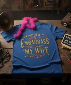 Blue t-shirt with gold glitter text that reads "I'm Just Here to Embarrass My Wife" in a decorative font