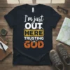 I'm Just Out Here Trusting God t-shirt with bold typography and mountain graphic, featuring a compass motif