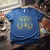 I'm Just A Girl quote in gold glittery font on a blue t-shirt, surrounded by laurel leaves and stars