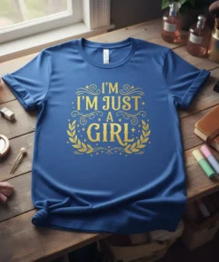 I'm Just A Girl quote in gold glittery font on a blue t-shirt, surrounded by laurel leaves and stars