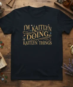 T-shirt with "I'm Kaitlyn Doing Kaitlyn Things" in decorative gold and teal lettering, featuring stars and swirls
