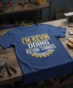Blue t-shirt with yellow and white text reading "I'M KEVIN DOING KEVIN THINGS KEVIN THINGS" in a workshop setting