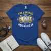 Blue t-shirt with white and gold text: "I'm Living With a Heart Transplant & Rocking It" and a heart graphic