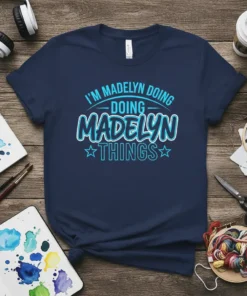 Navy t-shirt with "I'm Madelyn Doing Doing Madelyn Things" in bright blue and white text, featuring playful typography