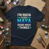 Navy t-shirt with white and blue gradient text "I'M MAYA DOING MAYA DOING MAYA *THINGS*" for personalized name gifts