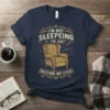 Navy t-shirt with vintage-style text "I'm Not Sleepeing I'm Just Resting My Eyes" and an illustration of a tufted armchair