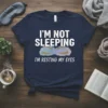 Navy t-shirt with white text "I'm Not Sleeping I'm Resting My Eyes" and a graphic of closed eyes with gold