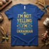 Blue t-shirt with yellow and blue text "I'm Not Yelling I'm Ukrainian" in a decorative font, featuring Ukrainian folk art