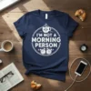 I'm Not A Morning Person quote on a navy t-shirt with a grumpy coffee cup and alarm clock graphics