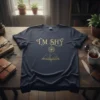 Dark navy t-shirt with gold glitter text "I'm SHY" above a gold line drawing of an open book with a