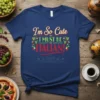 Navy blue t-shirt with the text "I'm So Cute I MUST BE ITALIAN!" in decorative fonts, surrounded by grape vines