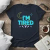 Navy t-shirt with "I'M TIRED" text in bold blue and yellow letters, featuring a crescent moon and star graphic