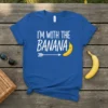 Blue t-shirt with white text "I'm With The Banana" and a smiling banana graphic with an arrow