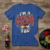 Blue t-shirt with red and cream retro text saying "I'M A SUCKER FOR YOR YOU" and hands holding a heart