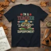 I'M A TEACHER What's your SUPERPOWER? quote on a navy t-shirt with apples, books, globe, and pencils graphic