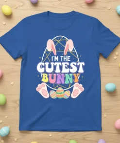 Blue t-shirt with the text "I'M THE CUTEST BUNNY" in colorful lettering, featuring bunny ears, feet, and decorated Easter eggs