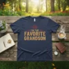 Navy t-shirt with "Official I'm The Favorite Grandson" text in distressed gold and red font, featuring vintage style accents