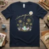 Navy t-shirt with the word "imagine" in gold script, adorned with dandelions, crystals, and a daisy graphic