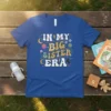 Retro groovy t-shirt with "In My Big Sister Era" text, stars, moons, and flowers in pastel colors