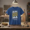 Blue t-shirt with "In My Bonus Dad Era" text in retro wavy font, featuring gear graphics and a heart