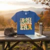 Retro "In My Boone Era" text design with mountains and trees on a blue t-shirt