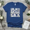 In My Bride Era t-shirt design with retro font, engagement rings, and floral accents in white and gold