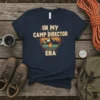 In My Camp Director Era text design with mountain and campfire graphic, retro style, on a navy t-shirt