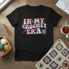 Retro "In My Crochet Era" text design with crochet hook and yarn graphic, featuring pastel colors on a black t-shirt
