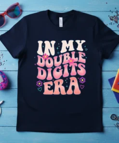 In My Double Digits Era text design with pink and orange wavy font and floral accents on a navy t-shirt
