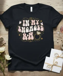 Black t-shirt with "IN MY ENGAGED R&A" in retro wavy font, surrounded by gold swirls, butterflies, and a diamond ring