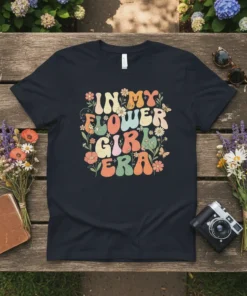 In My Flower Girl Era text with colorful retro flowers and butterflies graphic on a black t-shirt