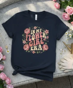 In My Flower Girl Era text with floral graphics on a navy t-shirt