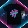 In My Gender Keeper Era neon text design with baby footprints on a black t-shirt