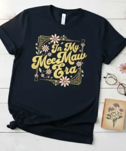 Navy t-shirt with "In My Mee Maw Era" in gold glitter font, surrounded by pink and white flowers