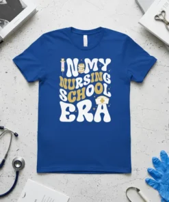 In My Nursing School Era text design with syringe, books, and nurse cap graphics on a blue t-shirt