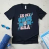 Retro "In My Swim Mom Era" text design with a swimming graphic, stars, and flowers on a navy t-shirt