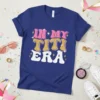 Retro groovy "In My Titi Era" text design with pink, gold glitter, and white lettering on a blue t-shirt