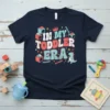Retro "In My Toddler Era" text with a cute dinosaur and building blocks graphic on a navy t-shirt